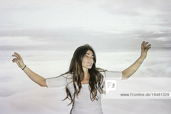 Carefree woman with arms outstretched over projection of clouds on wall
