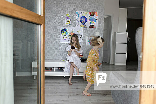 Girl playing with sister using smart phone in background