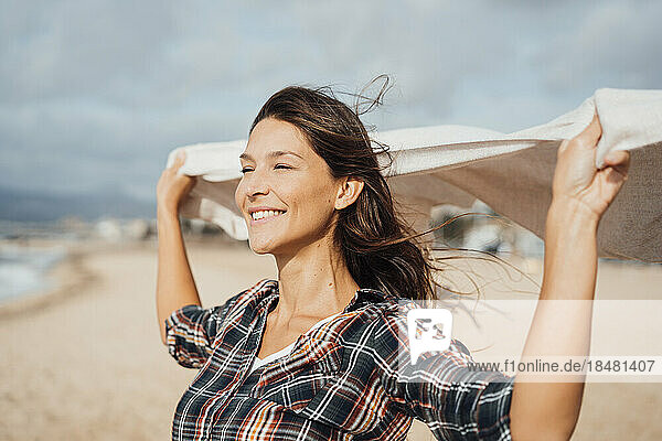 Smiling woman holding scarf and enjoying at beach