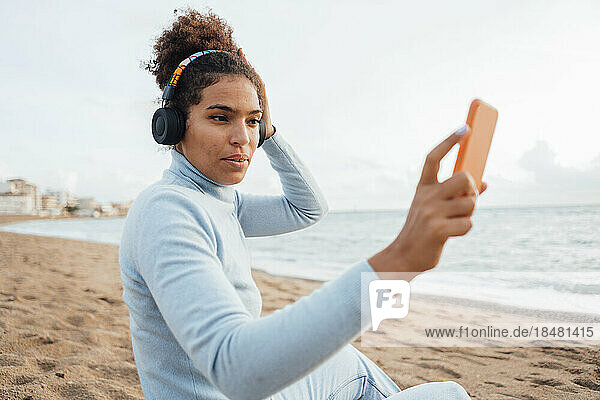 Young woman taking selfie using smart phone and listening to music through headphones at beach