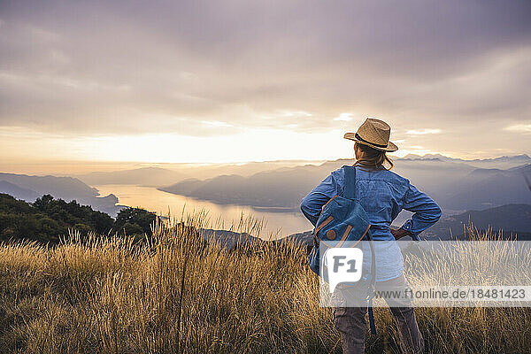 Reife Frau mit Hut steht bei Sonnenuntergang mit Rucksack