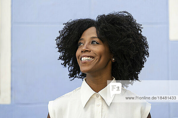 Thoughtful smiling woman with Afro hairstyle in front of wall