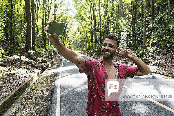 Happy man showing peace sign gesture and taking selfie in front of trees