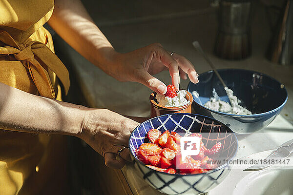 Hands of woman dipping strawberries in cream at kitchen