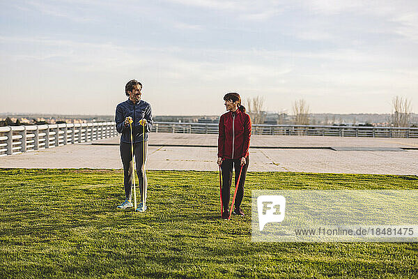 Mature couple exercising with resistance bands in park on sunny day