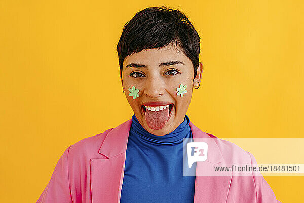 Young woman sticking out tongue against yellow background