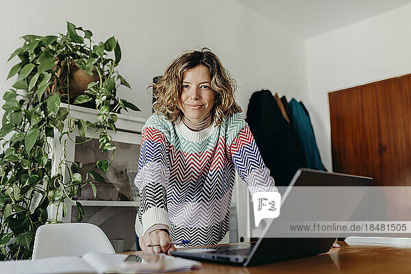 Smiling freelancer standing at laptop on table