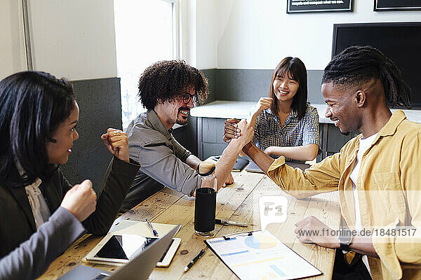 Businesswomen cheering colleagues doing arm wrestling at office