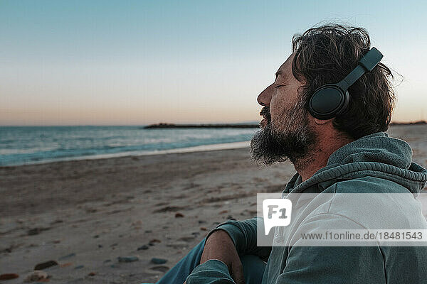 Mature man wearing headphones listening to music sitting at beach
