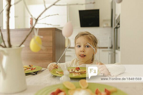 Cute girl eating pancakes for breakfast at home