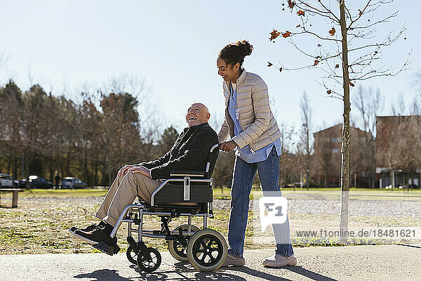 Woman assisting senior man on wheelchair in park
