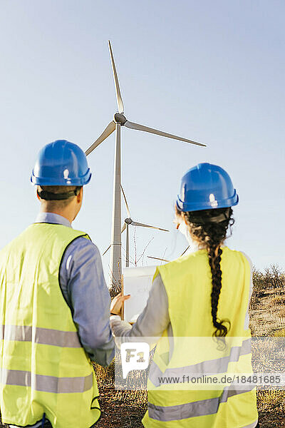 Engineers discussing over wind turbines on sunny day
