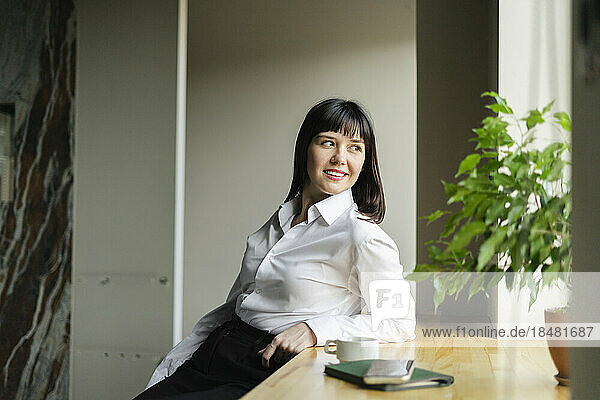 Smiling brunette businesswoman leaning on windowsill in office