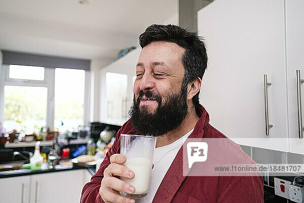 Lächelnder Mann genießt ein Glas Milch in der heimischen Küche