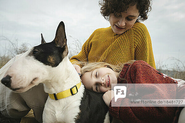 Daughter relaxing on mother's lap with Bull Terrier dog