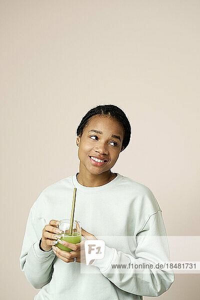 Contemplative woman holding green smoothie in front of wall