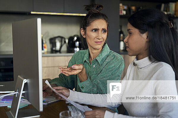 Freelancers discussing over document at desk in home office