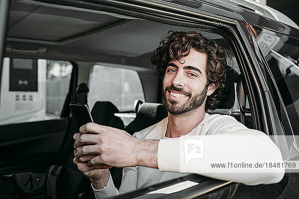 Smiling man with smart phone traveling in car