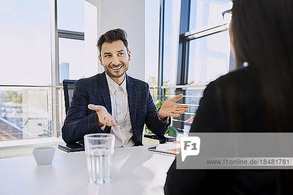 Happy businessman gesturing in meeting with colleague at office