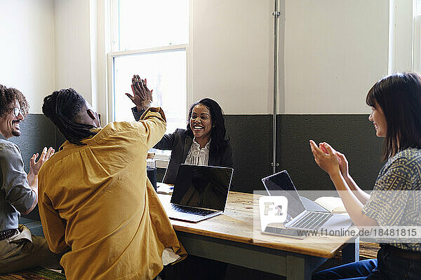 Zufriedene Geschäftskollegen geben High-Five am Schreibtisch im Büro