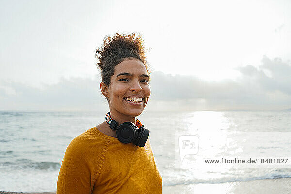 Happy woman with wireless headphones standing at beach