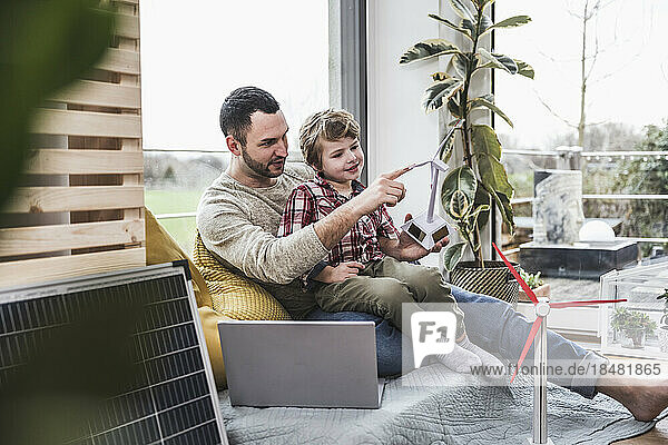 Father touching wind turbine model with son sitting at home