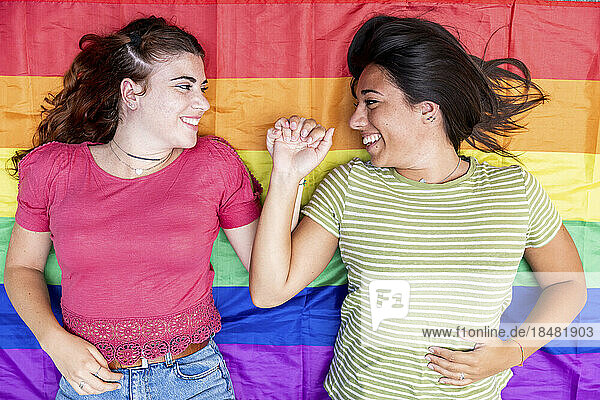 Glückliches lesbisches Paar  das Händchen hält und auf einer regenbogenfarbenen Flagge liegt