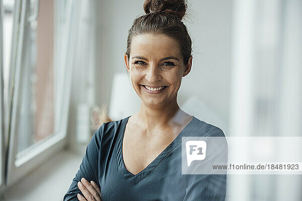 Happy businesswoman with arms crossed standing in home office