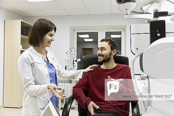 Smiling ophthalmologist talking to patient sitting in clinic