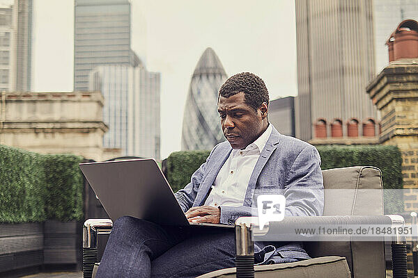 Businessman working over laptop sitting on armchair
