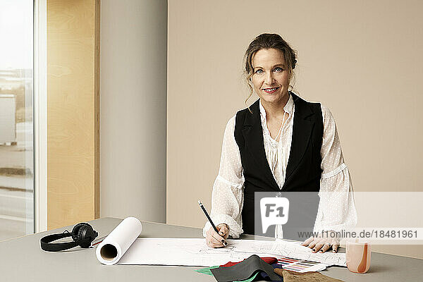 Mature fashion designer with sketch on desk at studio