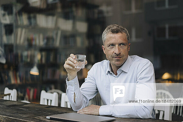 Businessman with glass of drinking water sitting at cafe