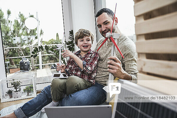 Father and son playing with wind turbine models sitting at home