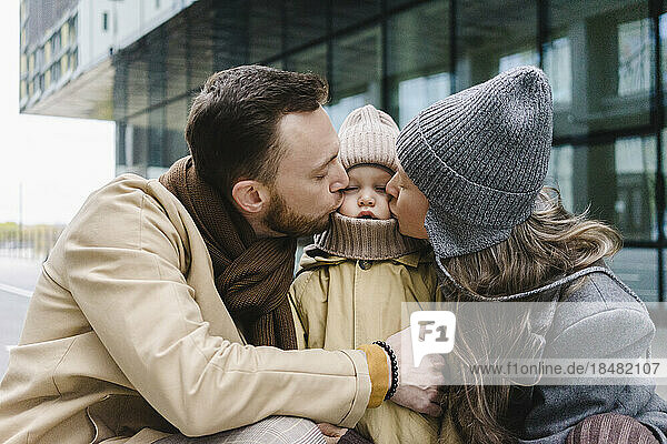 Mutter und Vater küssen ihren Sohn vor dem Gebäude