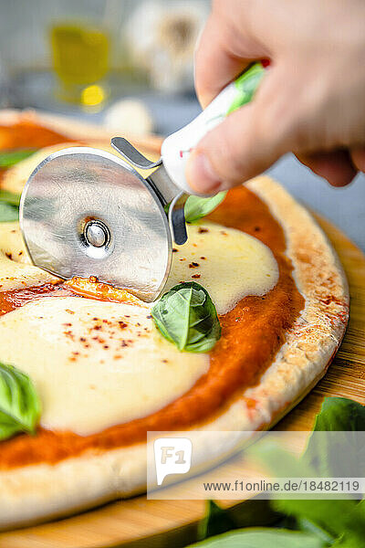 Hand of woman cutting pizza with cutter on table