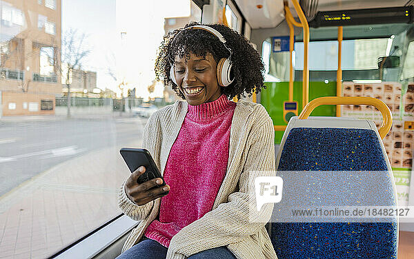 Happy woman wearing wireless headphones using smart phone in tram
