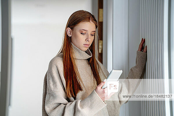 Teenager using smart phone standing by radiator at home