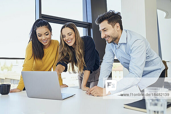 Zufriedene Geschäftskollegen arbeiten am Laptop und lehnen sich an den Schreibtisch im Büro