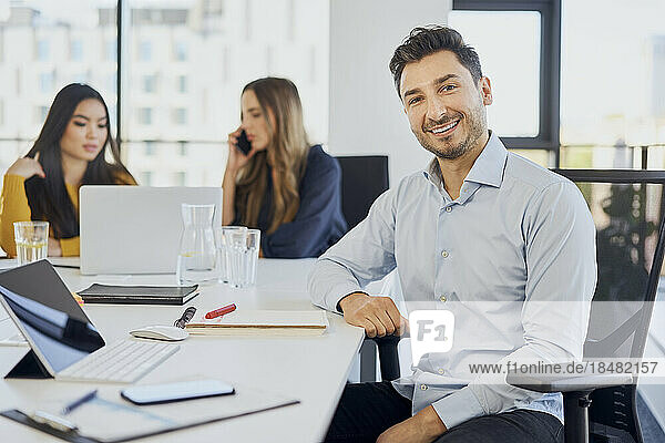 Happy businessman sitting on chair by desk at workplace
