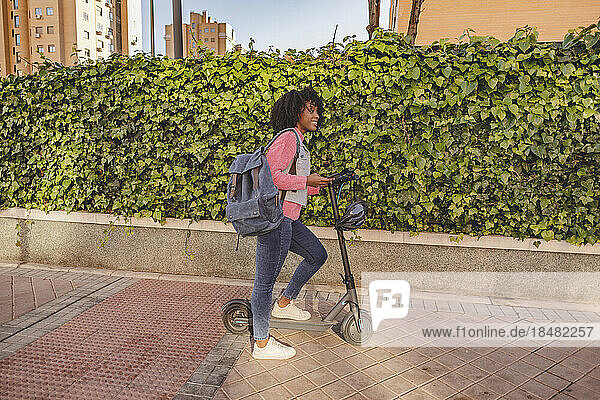Young woman with electric push scooter standing on footpath