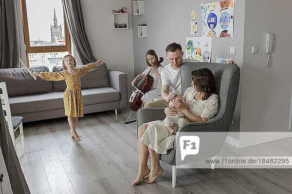 Parents holding baby boy with girls playing musical instrument in background