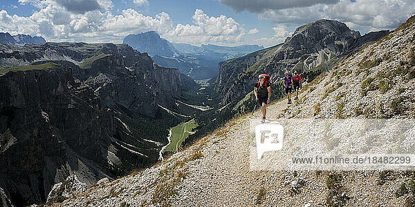 Women and man hiking towards Rifugio Puez on sunny day at Dolomites  Italy