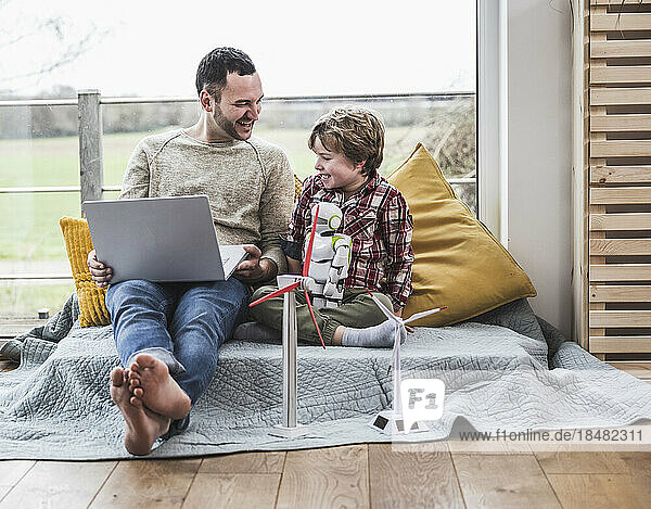 Excited father and son sitting with laptop on couch with wind turbines