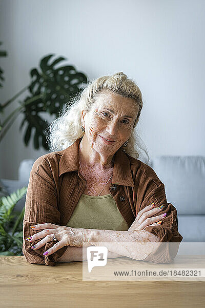 Smiling senior woman with arms crossed at home