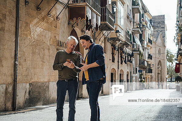 Father and son using smart phone standing on street