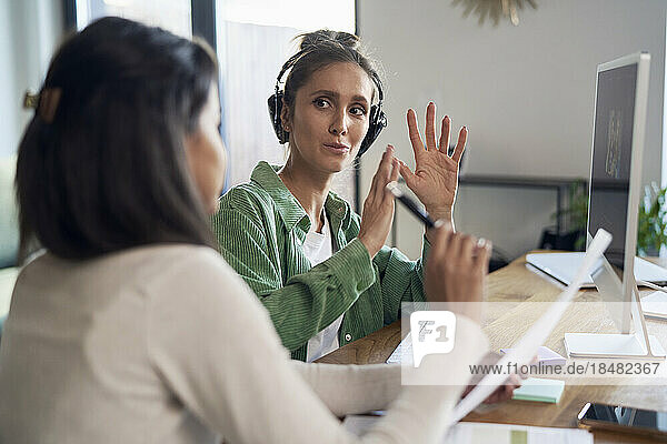 Businesswoman with headphones explaining colleague at home office