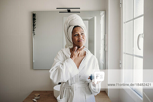 Woman applying moisturizer on face in bathroom