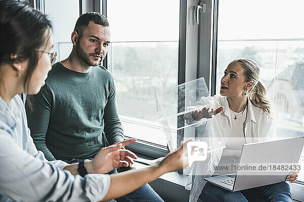 Businesswoman explaining glass cubicle to colleagues in meeting at office