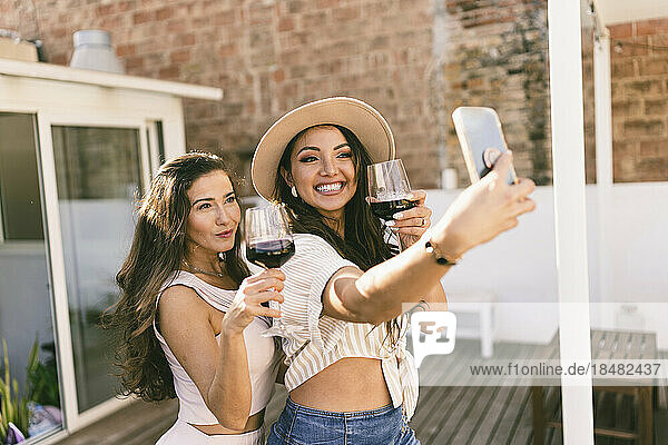 Friends with wine glasses taking selfie through smart phone