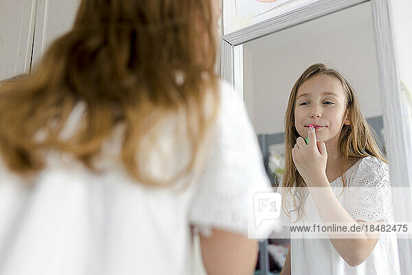 Smiling girl applying lipstick looking in mirror at home